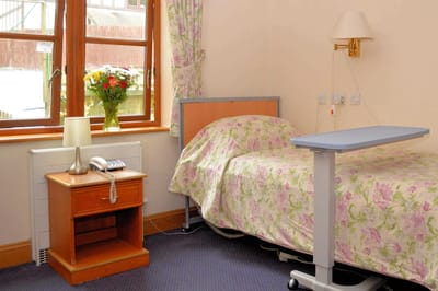 Cozy resident room with floral bedding and lamp.
