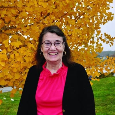 Smiling woman in front of a colorful autumn tree.