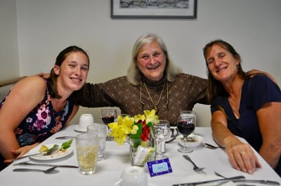 Three women smiling at a dining table with food.