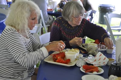 Two women enjoying a lobster dinner outdoors.