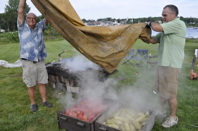 Two men cooking outdoors with food.