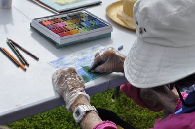Senior woman painting outside with pastels.