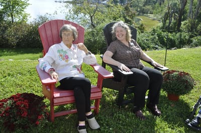 Two women sitting in chairs outdoors by a garden.
