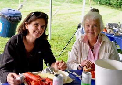 Two women enjoying a meal outdoors at a gathering.