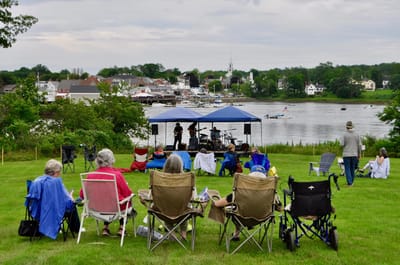 Residents enjoying an outdoor musical event by the water.