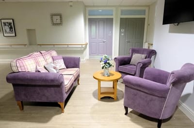 Cozy common area with purple seating and flowers.