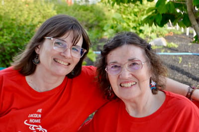 Two women smiling outdoors in red shirts.