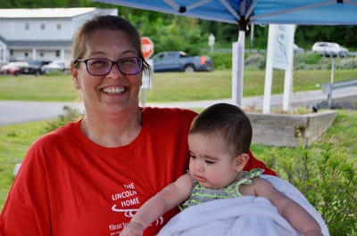 Smiling staff member holding a baby outdoors.