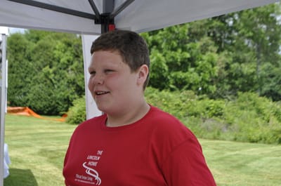 A young boy smiling outdoors at an event.