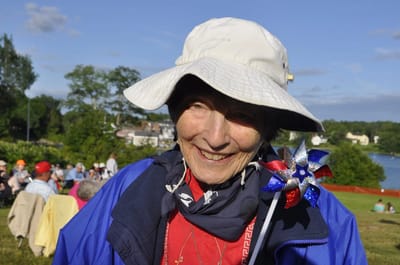 Elderly woman enjoying an outdoor event by the lake.