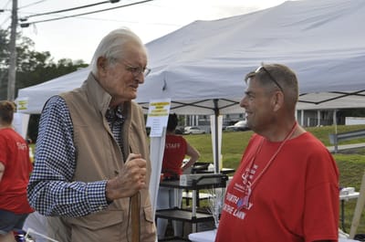 Two elderly men chatting at an outdoor event.