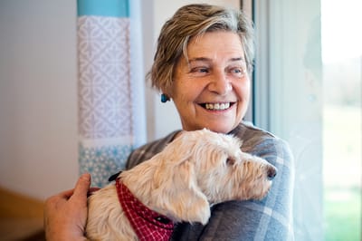A smiling resident holding a small dog indoors