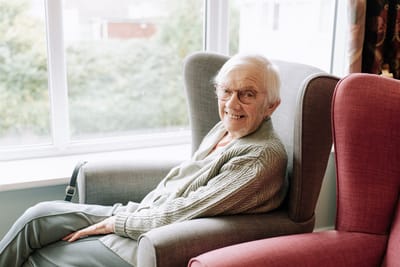 A resident smiling in a cozy chair by a window