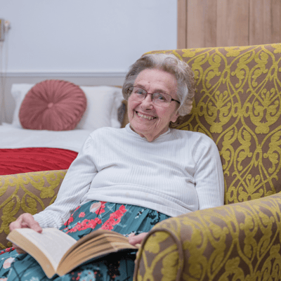 Senior resident reading a book in a cozy chair.