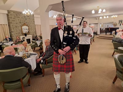 Piper in tartan suit performing in dining area.