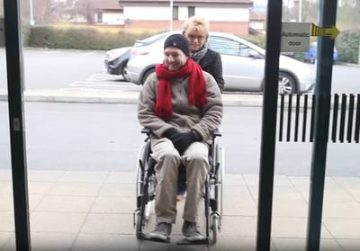Person in a wheelchair assisted by a caregiver.