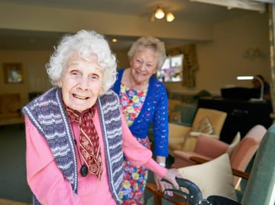 Two smiling elderly women interacting in a common area.