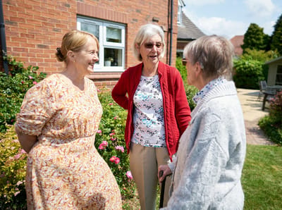 Three women conversing in a garden setting.