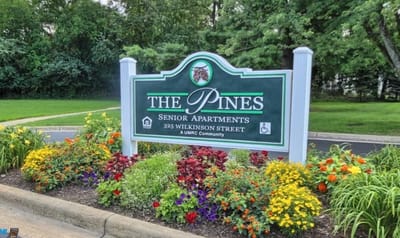 Sign for The Pines Senior Apartments surrounded by flowers