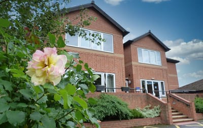 Exterior view of Abbeyfield Middleton House with garden roses.