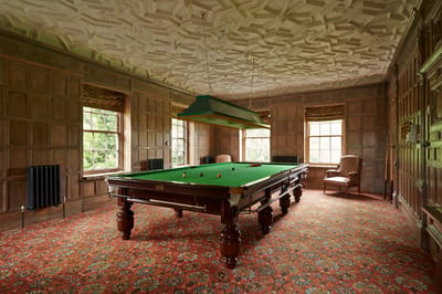 A billiards room with green table and ornate ceiling