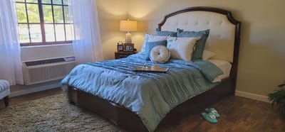 A well-decorated private resident room with a bed and lamp