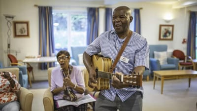 Resident playing guitar while others sing in a common area