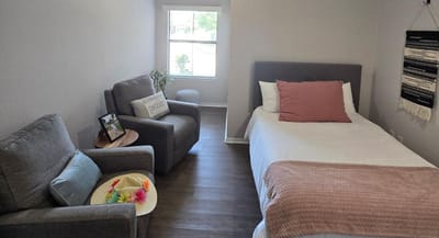 Brightly lit private resident room with a bed and seating area