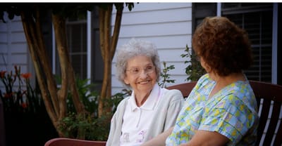 A resident and staff member chatting outside on a bench
