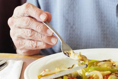 An elderly hand holding a fork over a plate of food