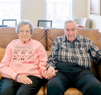 Two residents sitting together on a couch, holding hands