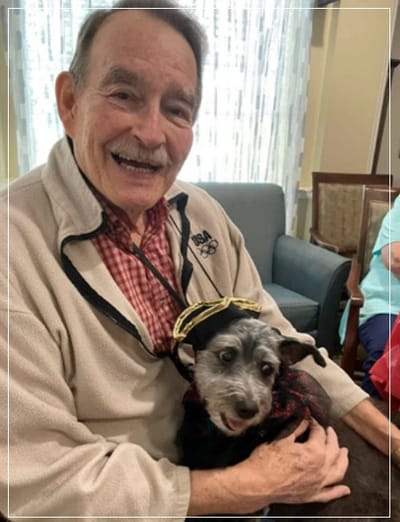 Resident smiling with a dog in a cozy room