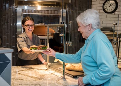A staff member serving food to a smiling resident