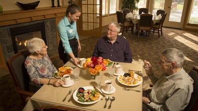 Residents enjoying lunch in a dining area with a staff member