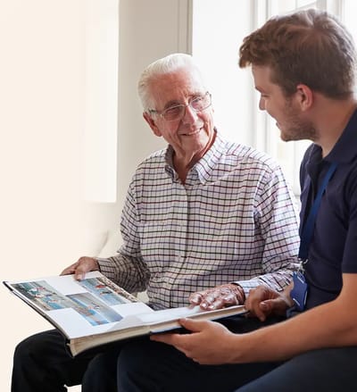 An elderly man looking at a photo album with staff member