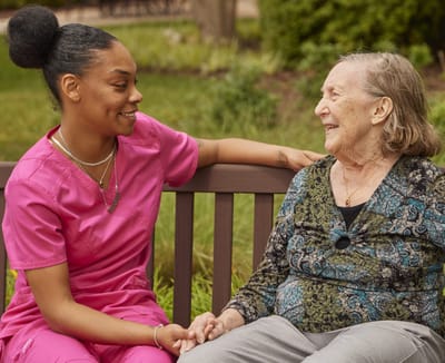 A staff member and resident enjoying conversation on a park bench