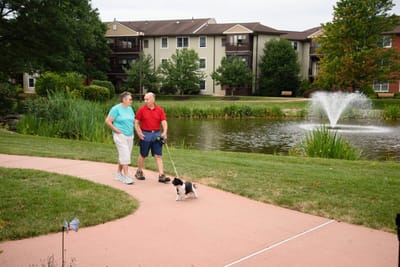 Monroe Village Assisted Living, nursing home in Monroe Township, NJ — Couple walking a dog by a landscaped pond