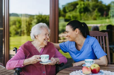 Monroe Village Assisted Living, nursing home in Monroe Township, NJ — Woman caring for elderly resident with tea and smiles
