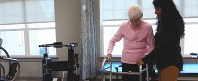 Staff helping a resident with a walker in a bright room