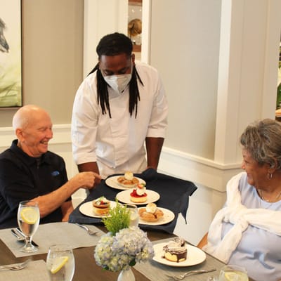 Residents enjoying dessert served by staff in the dining room