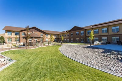 Exterior view of a senior living facility with gardens and seating areas.