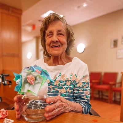 Resident proudly holding a handmade craft in an activity room