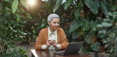 Senior woman using a laptop in a lush indoor garden.