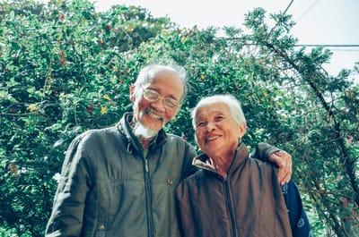 Elderly couple smiling outdoors in nature.
