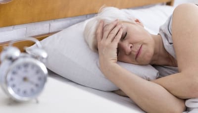 Senior woman resting in bed with alarm clock