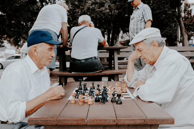 Two elderly men playing chess outdoors.