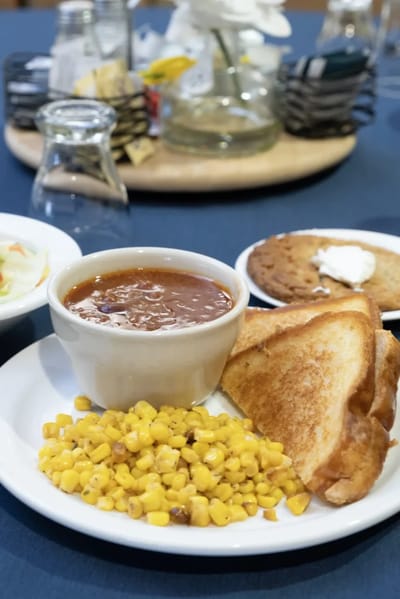 A plate of food including soup, toast, corn, and dessert.