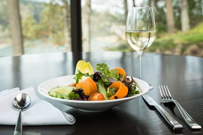 A colorful salad with a glass of white wine on a table