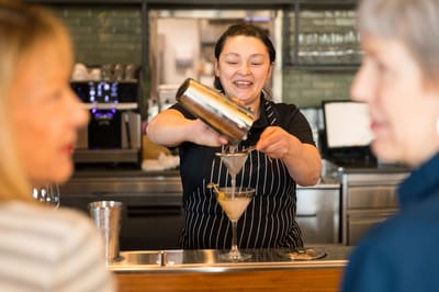 Bartender serving cocktails to residents in a lively setting