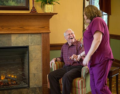 A resident enjoying time with staff next to a fireplace